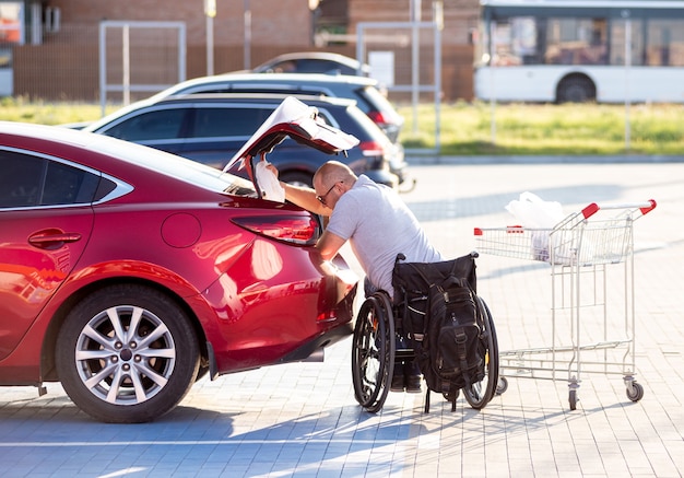 La persona con disabilità fisica mette gli acquisti nel bagagliaio di un'auto nel parcheggio di un supermercato