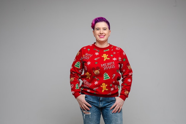 写真 ポケットに指を入れてカメラに向かって微笑んでいるクリスマスセーターの短い染めの髪の人。新年のコンセプト