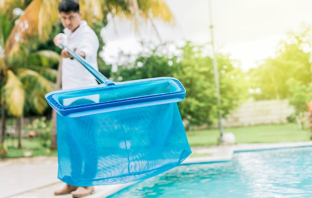 Person with skimmer cleaning pool Man cleaning the pool with the Skimmer A man cleaning pool with leaf skimmer Hands holding a skimmer with blue pool in the background