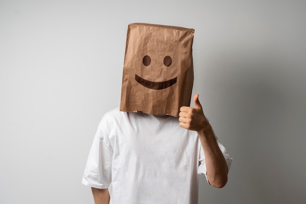Человек с большим пальцем вверх и счастливой улыбкой на бумажном пакете на голове