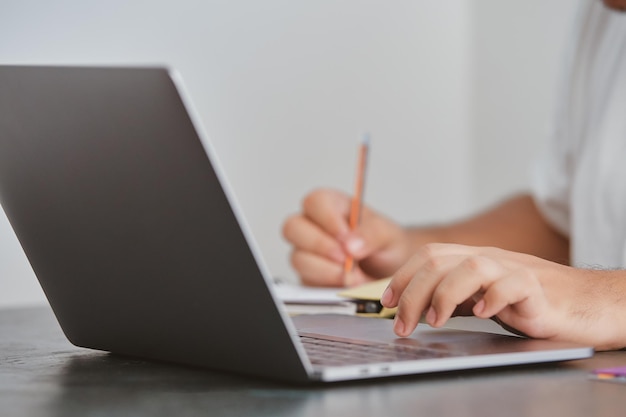 A person writing on a laptop with a pencil.