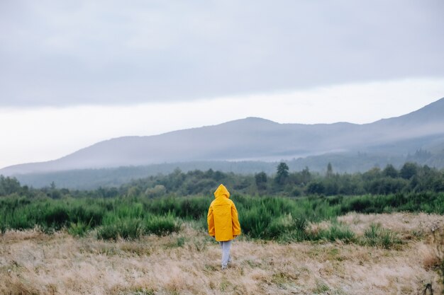 Person in a yellow raincoat with his hands raised stands in the rain