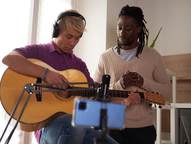 A personal afroamerican tutor explains to his asian student how to play studied chord correctly Musical education at home