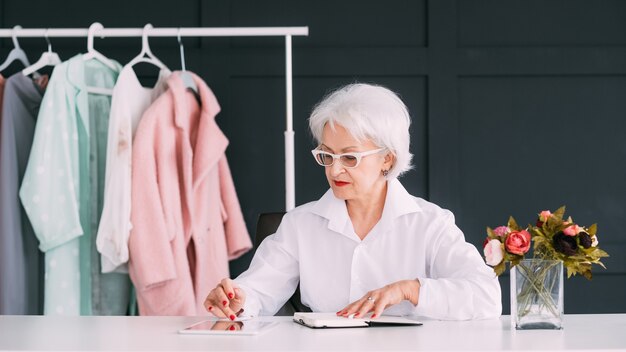 Personal fashion stylist. Successful money making business. Confident senior lady at workplace browsing tablet.