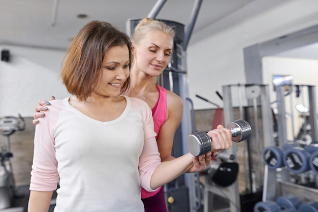 Personal fitness instructor helping summer woman exercising in health club.