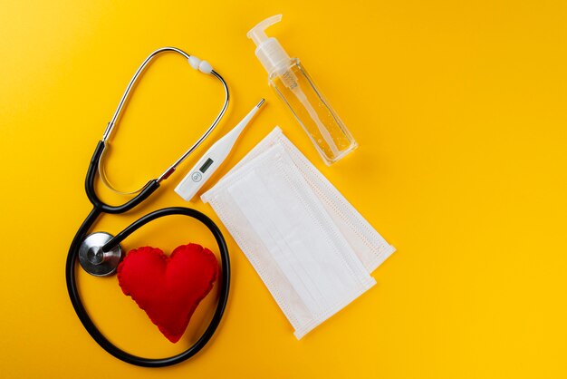 Personal hygiene equipment antiseptic gel, masks, thermometer and stethoscope. yellow wall.personal hygiene concept