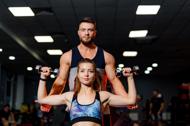 Il personal trainer maschile aiuta il cliente donna con esercizi fisici in palestra sfondo scuro palestra vista frontale del primo piano