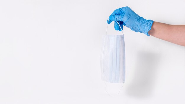 Персональная защита от простуды и вирусов. Рука медицинского работника в синих перчатках падает защитная маска на белом
