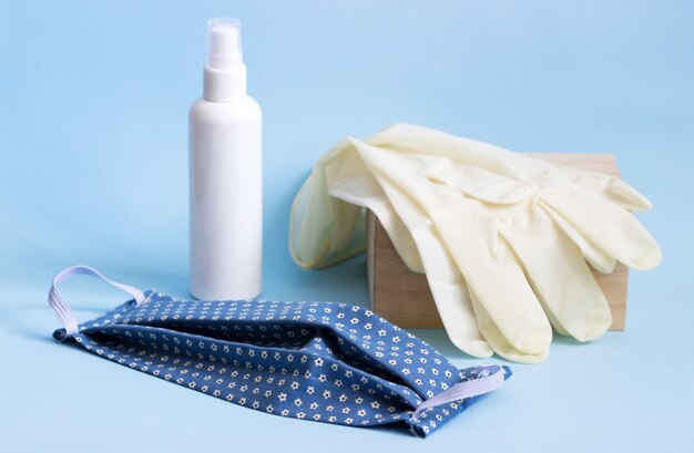 Personal protective equipment mask, gloves and disinfectant on a blue background.