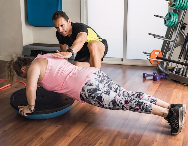 Personal trainer die een vrouw helpt evenwichtsoefeningen te doen terwijl ze push-ups doet in een sportschool