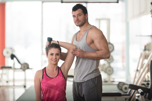 Personal Trainer die jonge vrouw toont hoe triceps te trainen Oefening met halter in een sportschool