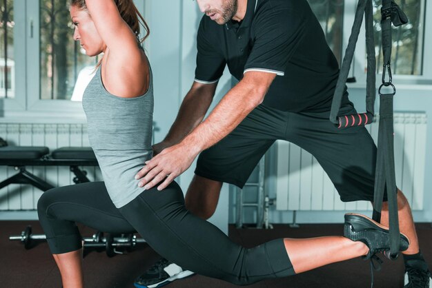 Personal trainer exercising on TRX with woman in the gym