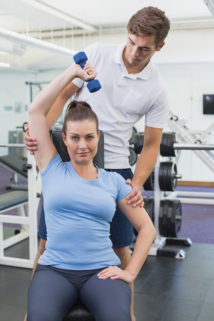 Personal trainer helping client lift dumbbell