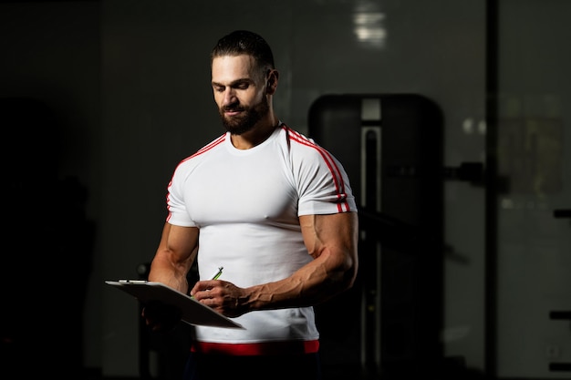 Personal Trainer maakt aantekeningen op het klembord in de sportschool van het fitnesscentrum