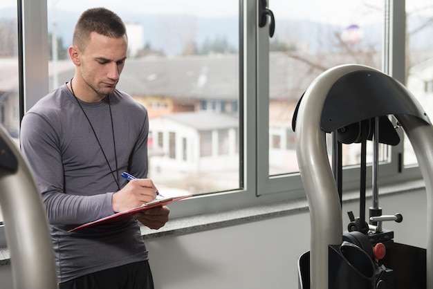 Personal trainer maakt aantekeningen terwijl de man zijn benen traint