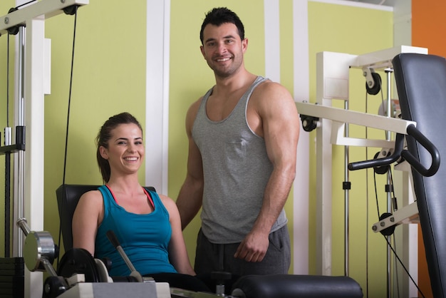 Personal Trainer Showing Young Woman How To Train Legs On Machine In The Gym