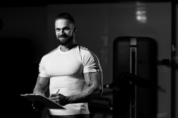 Personal Trainer Takes Notes On Clipboard In Fitness Center Gym