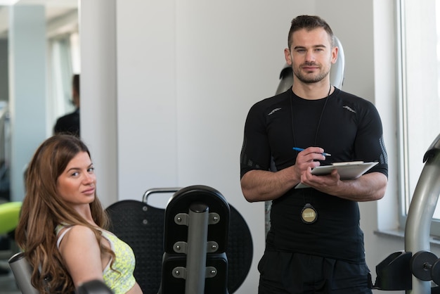 Photo personal trainer takes notes while woman exercising legs