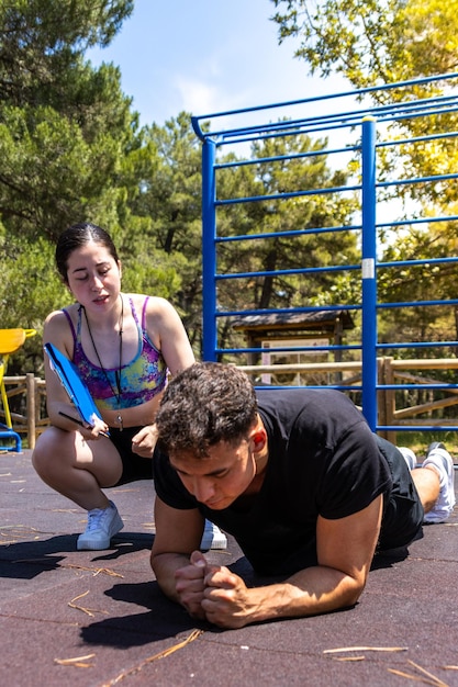 personal trainer woman guiding watching motivating and cheering a sporty man while doing plank exercises in a sport park