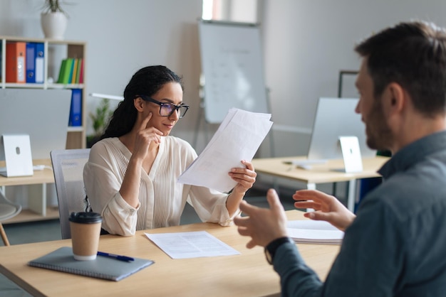 Personnel manager communicating with vacancy candidate reading resume during job interview at office