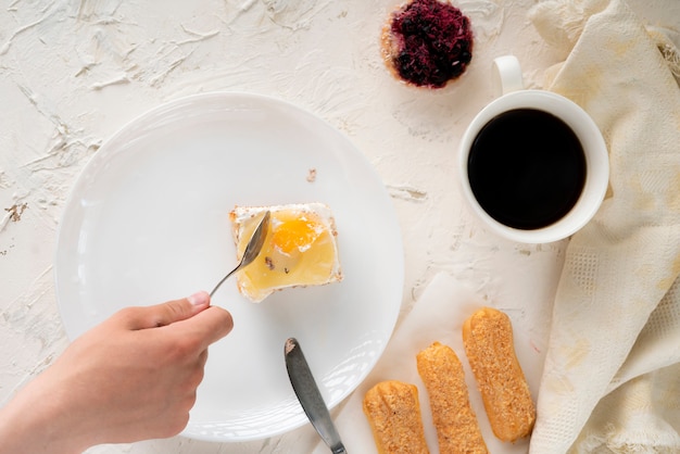 人の手がスプーンとフードナイフを握り、皿、食器、上面図の甘いケーキを食べる