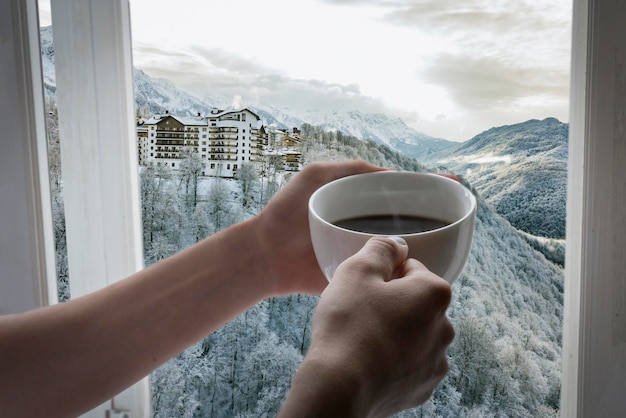 persons hands hold cup of hot coffe opposite from the window at winter season b