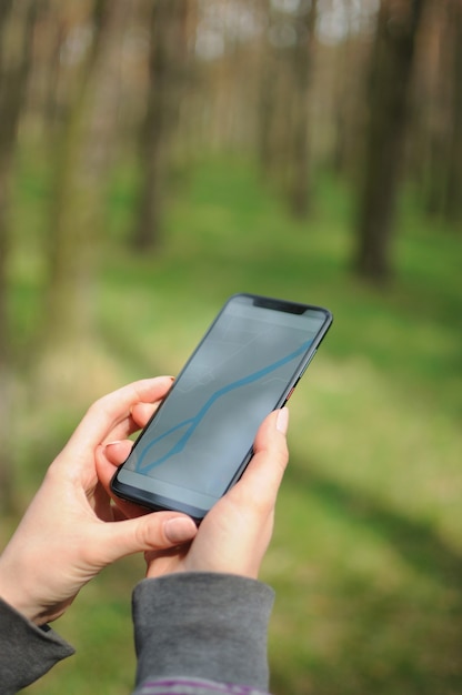 Persoon alleen zoekt pad via gps-navigator op smartphone in het bos in de lente