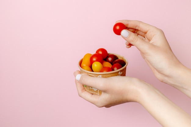 Persoon die een kom tomaten op een roze achtergrond houdt