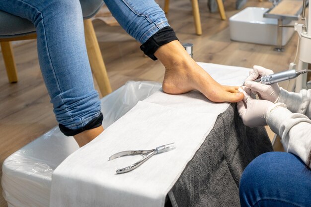 Persoon die een pedicure begint uit te voeren op een cliënt met een nagelpolijstmachine.