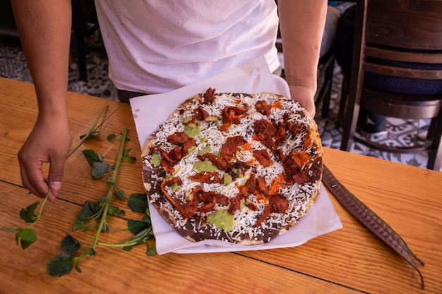 Foto persoon die een traditioneel mexicaans gerecht eet genaamd tlayuda, gemaakt van tortilla met bonen en vlees