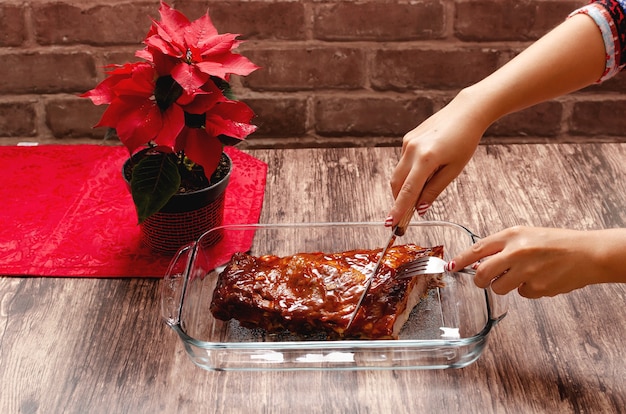 Persoon die gegrilde ribben snijdt met barbecuesaus op een houten tafel met poinsettia plant