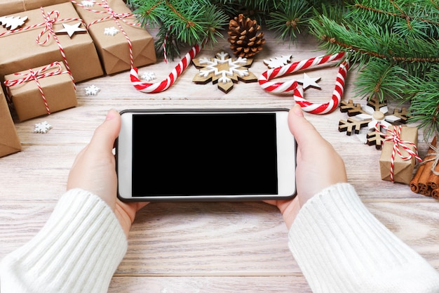 Persoon die in geopende smartphone op rustieke houten lijst schrijft die met Kerstmisdecoratie wordt behandeld