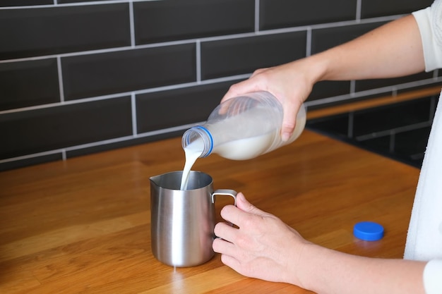 Persoon die melk in een stalen kruik giet en cappuccino maakt