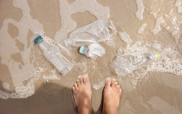 Persoon die met plastic flessenafval op het strand staat