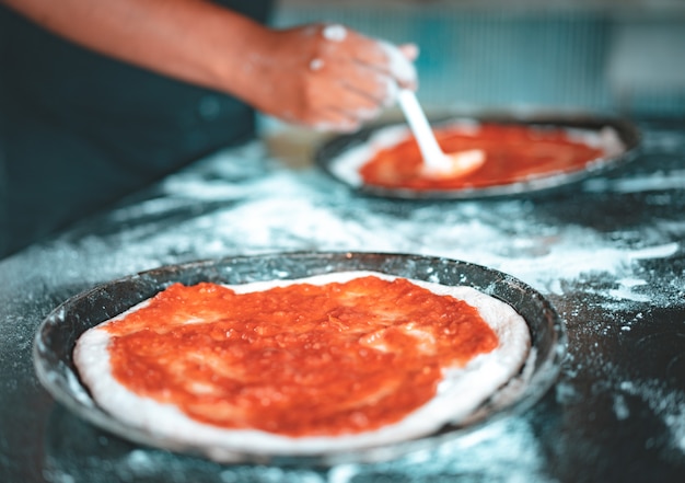 Persoon die saus op eigengemaakte pizza zet