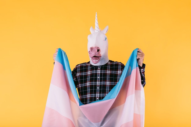 Persoon gekleed in een eenhoornmasker met een geruit overhemd met de vlag van het transseksuele collectief op een gele achtergrond concept van gay pride-transseksualiteit en lgtbq-rechten