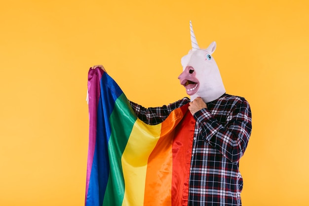 Persoon gekleed in eenhoornmasker met geruit hemd met lgtbq-regenboogvlag op gele achtergrond Concept van gay pride-transseksualiteit en lgtbq-rechten
