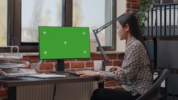 Persoon met behulp van computer met groen scherm in kantoor. Vrouw die geïsoleerde mockupachtergrond bekijkt met chromasleutel op monitor om opstartproject en marketingstrategie te plannen.