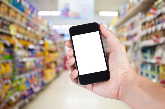 Persoon met behulp van smartphone witte scherm houder bij de hand met planken op de achtergrond in de supermarkt.