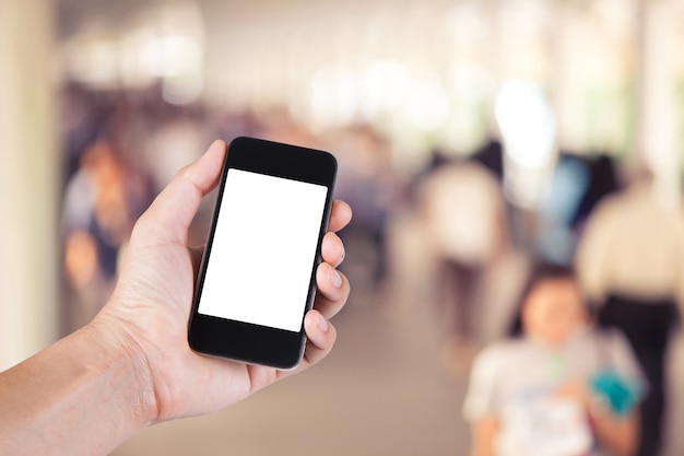 Persoon met behulp van smartphone witte scherm houder bij de hand met veel mensen lopen op skywalk in de grote stad.