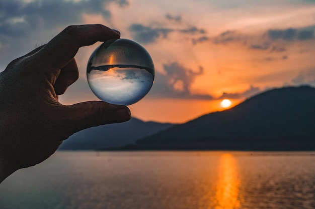 Persoon met een kristallen bol tegen de zee bij zonsondergang