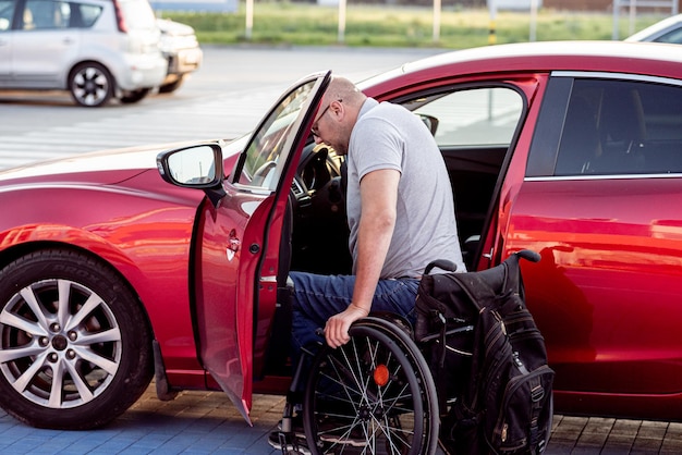 Persoon met een lichamelijke beperking stapt in rode auto vanuit rolstoel