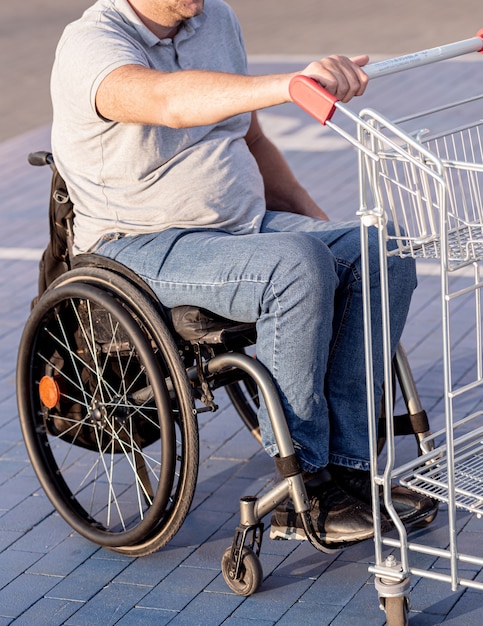 Persoon met een lichamelijke handicap die kar voor zich uit duwt bij supermarktparkeerplaats