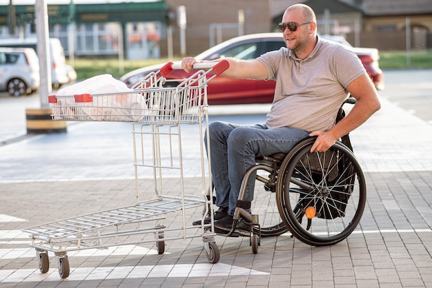 Persoon met een lichamelijke handicap die kar voor zich uit duwt bij supermarktparkeerplaats