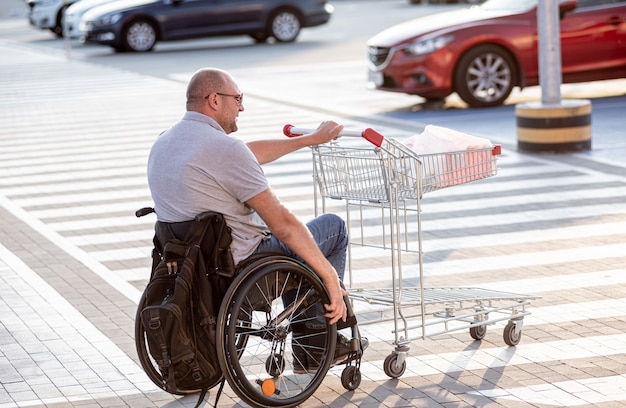 Persoon met een lichamelijke handicap die kar voor zich uit duwt bij supermarktparkeerplaats