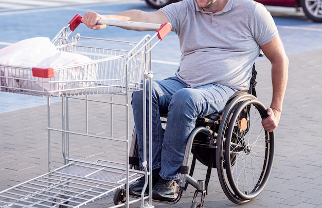 Persoon met een lichamelijke handicap die kar voor zich uit duwt op parkeerplaats supermarkt