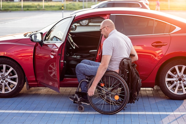 Persoon met een lichamelijke handicap die vanuit een rolstoel in de rode auto stapt