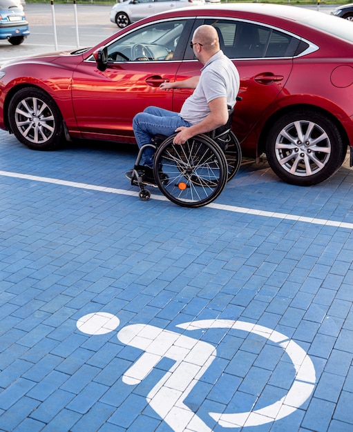 Persoon met een lichamelijke handicap die vanuit een rolstoel in de rode auto stapt