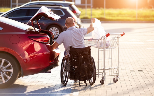 Persoon met een lichamelijke handicap doet aankopen in de kofferbak van een auto op een parkeerplaats van een supermarkt