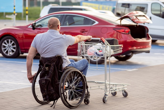 Persoon met een lichamelijke handicap duwt een kar naar een auto op een parkeerplaats van een supermarkt